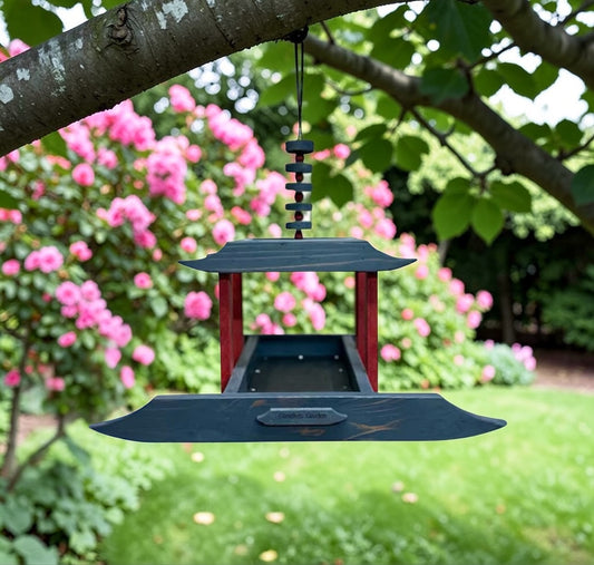 Hanging Asian styled bird feeder with pink flowers and greenery in the background