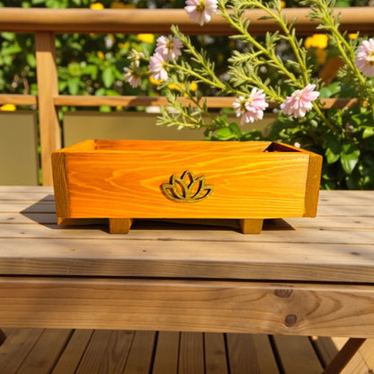 Wooden planter box with a lotus design on a wooden surface outdoors.