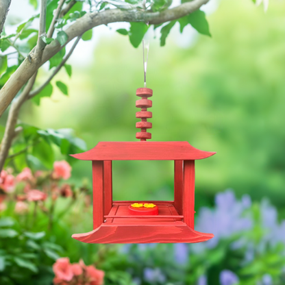 Red hummingbird feeder or Oriole/Bird feeder hanging from a tree branch with a blurred garden background