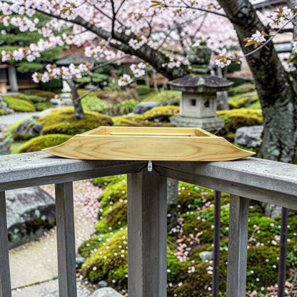 Cedar rail bird feeder on a railing with cherry blossom trees and a stone lantern in the background