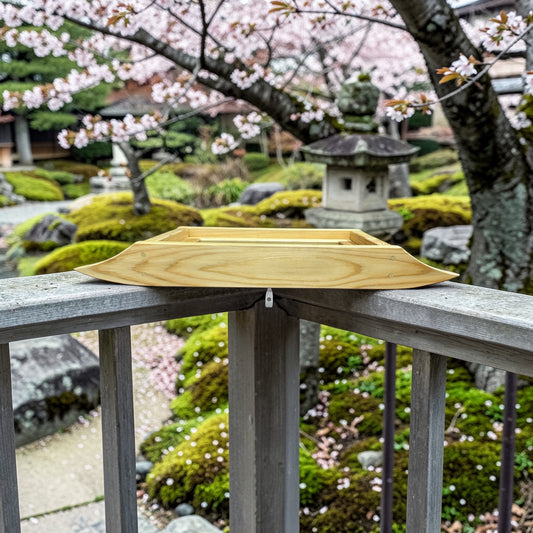 Cedar rail bird feeder on a railing with cherry blossom trees and a stone lantern in the background