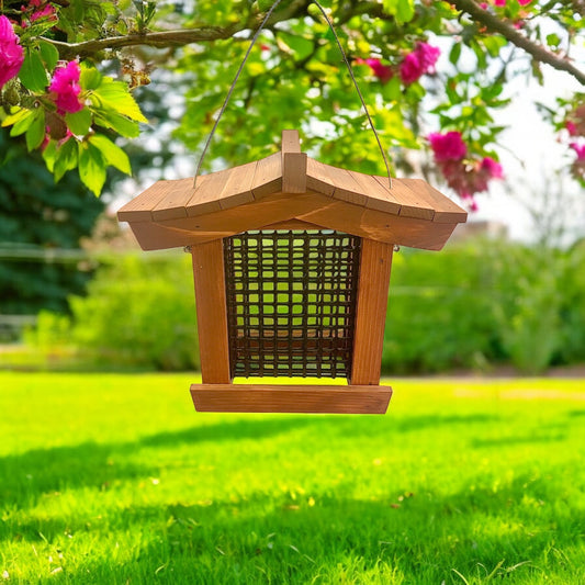 Wooden Asian style suet feeder hanging in a garden with green grass and pink flowers.