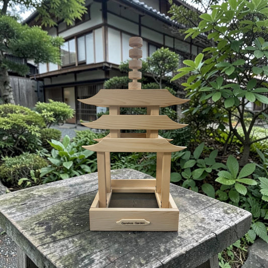 Wooden pagoda-shaped bird feeder on a stone surface with greenery and traditional building in the background