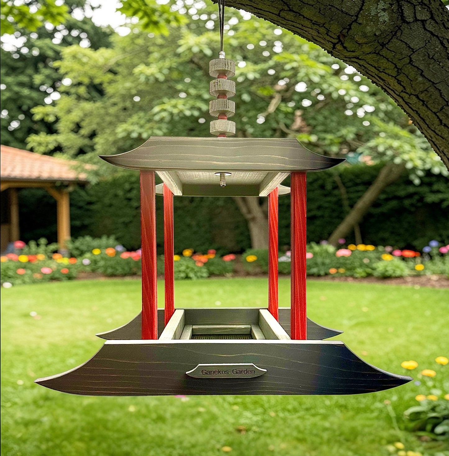 Asian garden bird feeder in a garden setting with trees and flowers in the background.