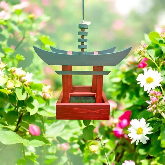 Decorative bird feeder shaped like a traditional Japanese Torii Gate hanging among flowers and greenery.