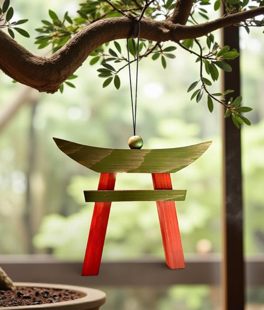 Wooden torii gate ornament hanging from a branch with green leaves.