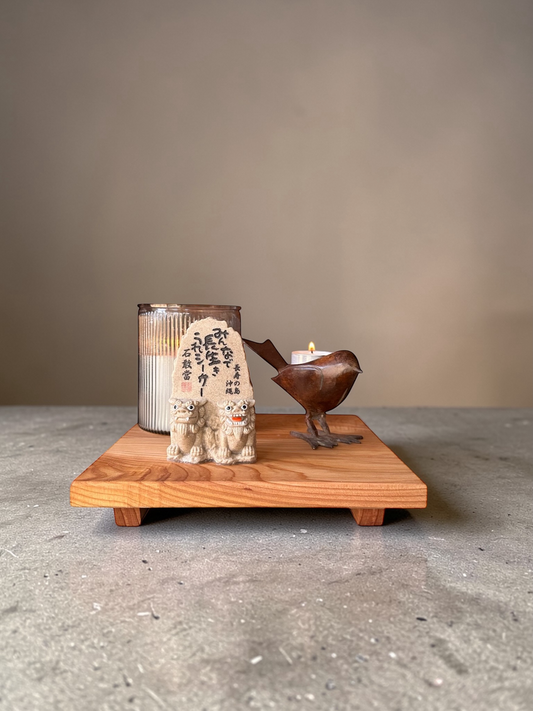 Decorative items including a candle, sculpture, and stone on a wooden stand against a plain background.